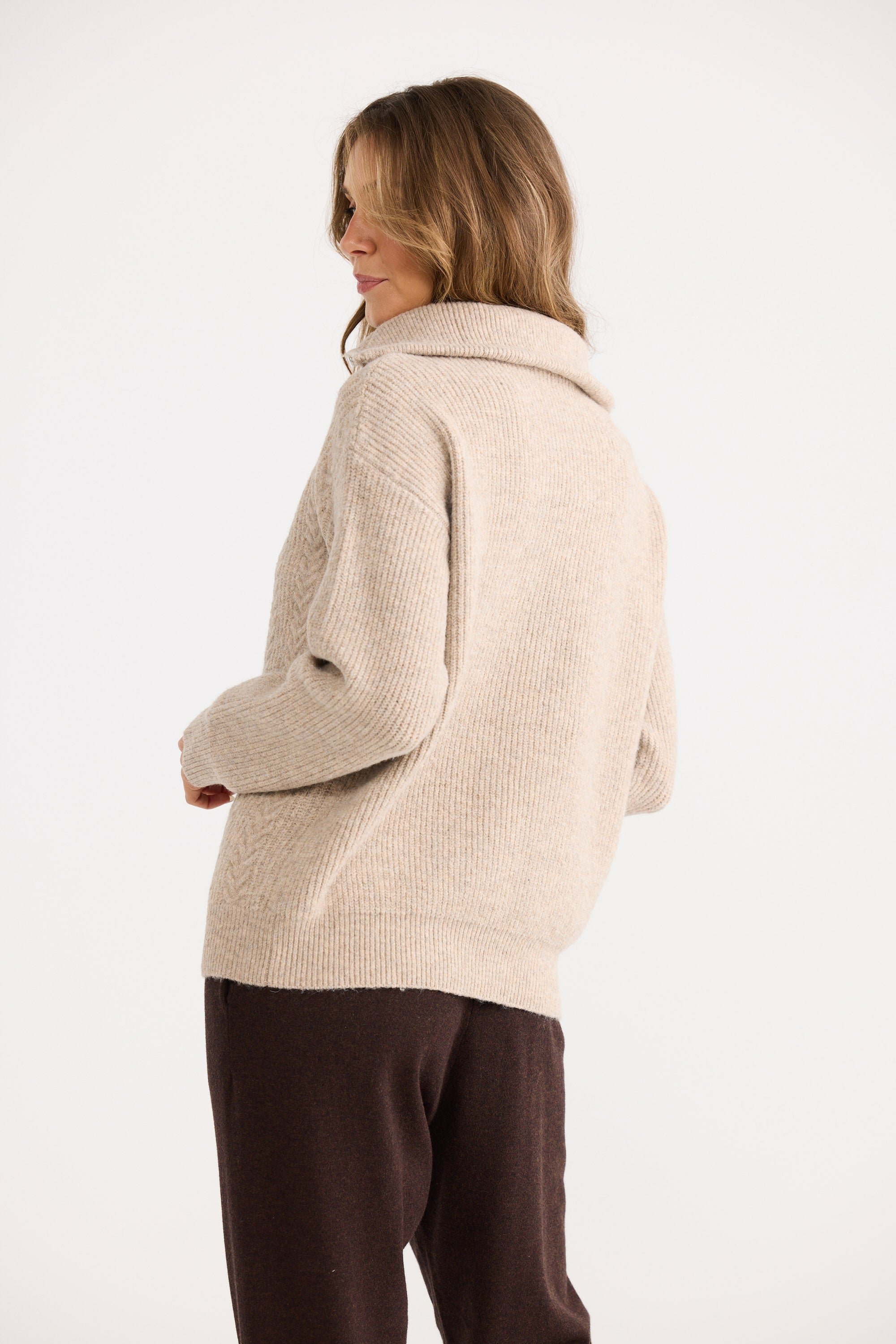 Woman wearing a beige knitted sweater and brown pants on a white background