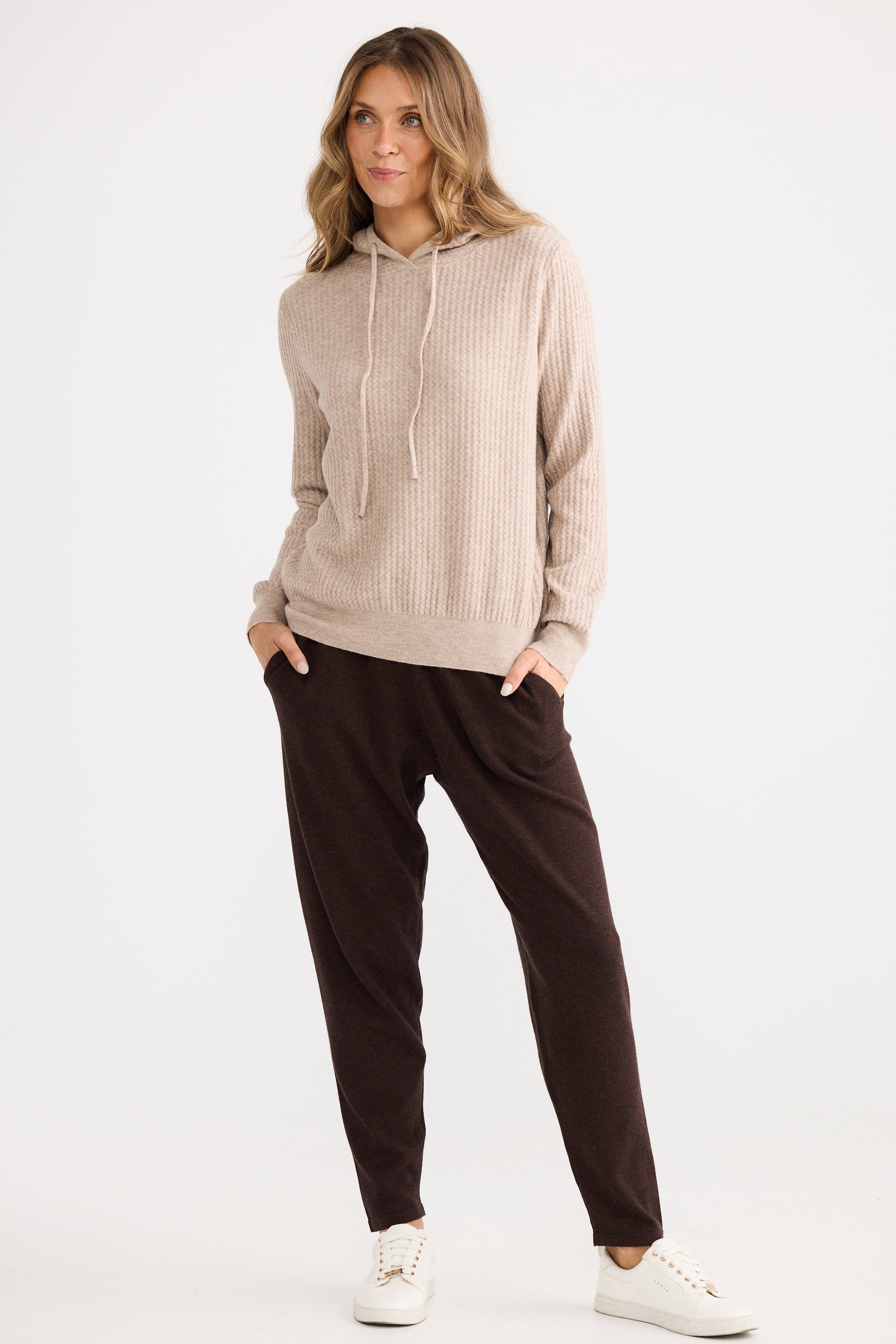 Woman wearing a beige sweater and brown pants on a white background