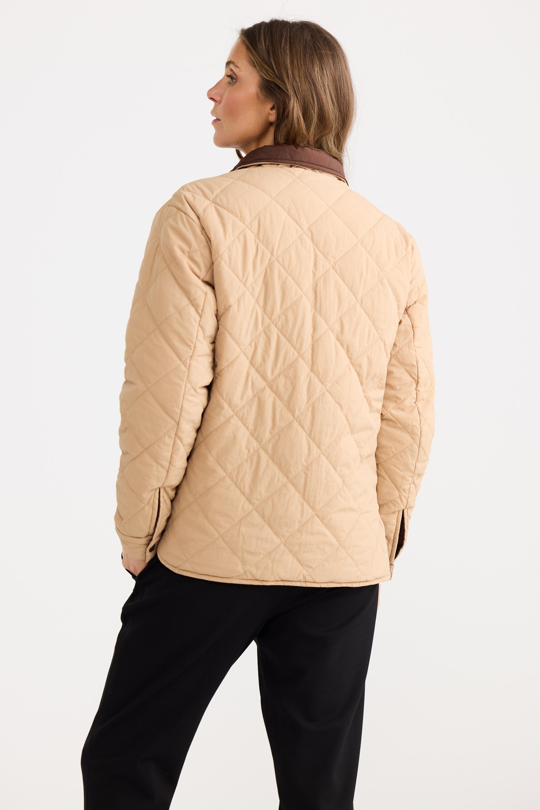 Woman wearing a beige quilted jacket on a white background