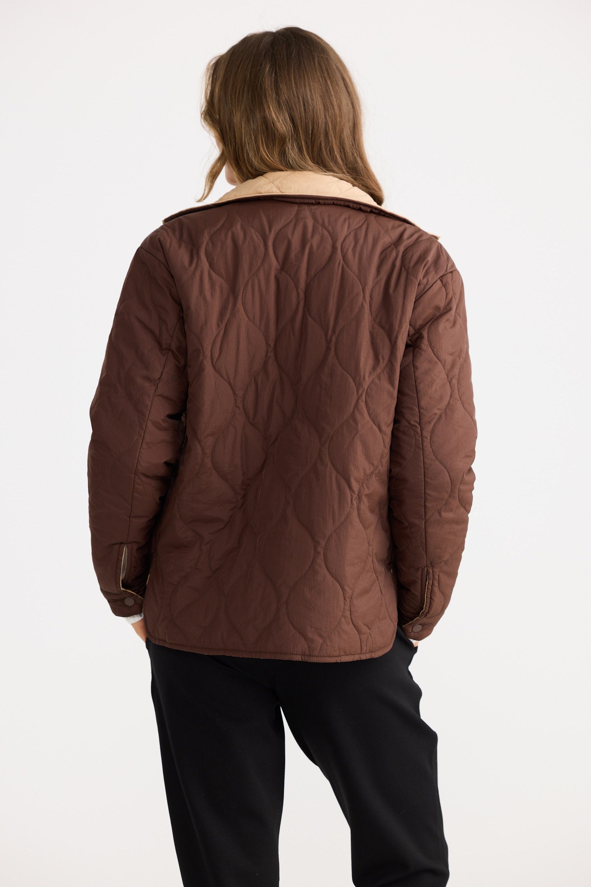 Person wearing a brown quilted jacket on a white background
