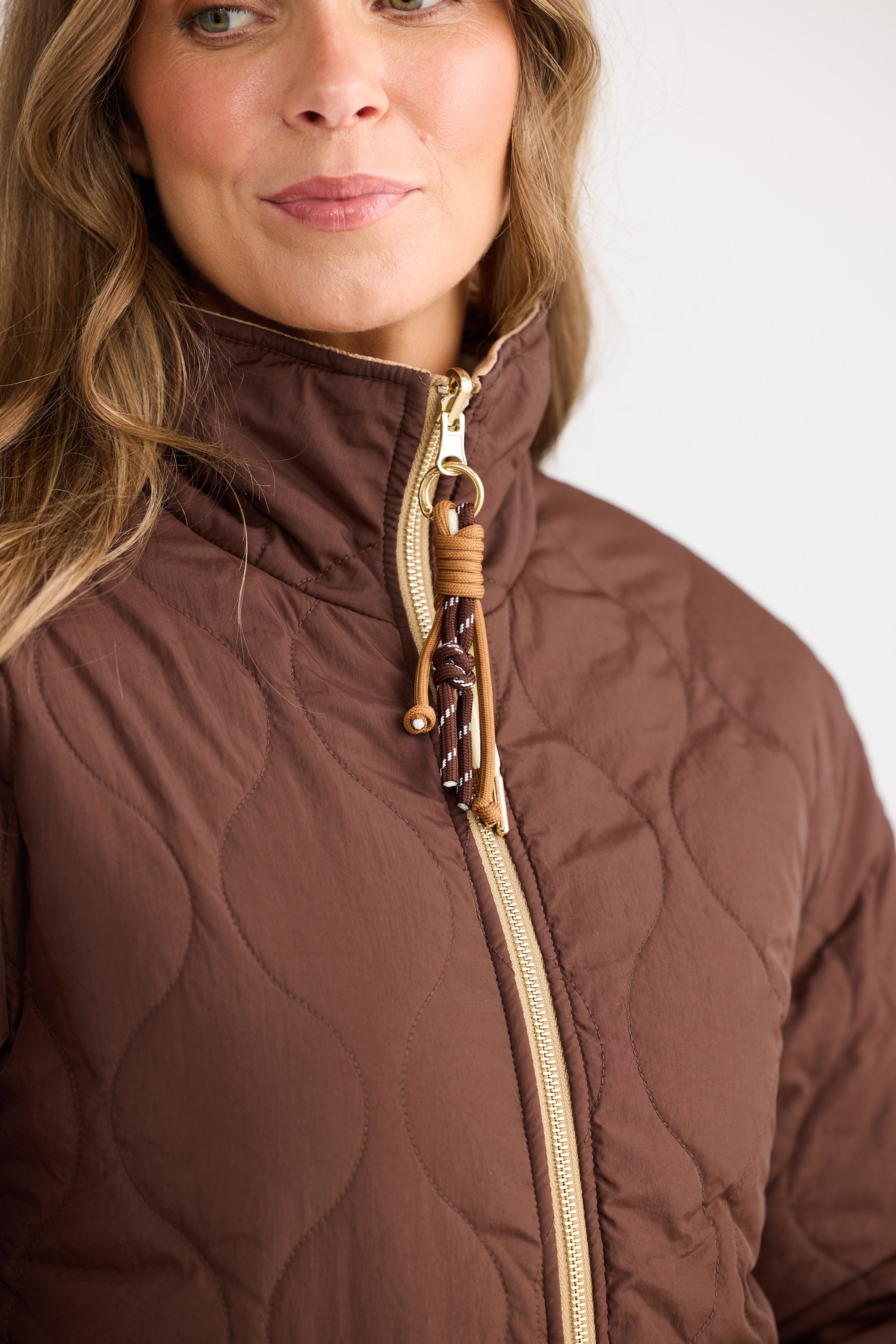 Close-up of a person wearing a brown quilted jacket with a decorative zipper pull.