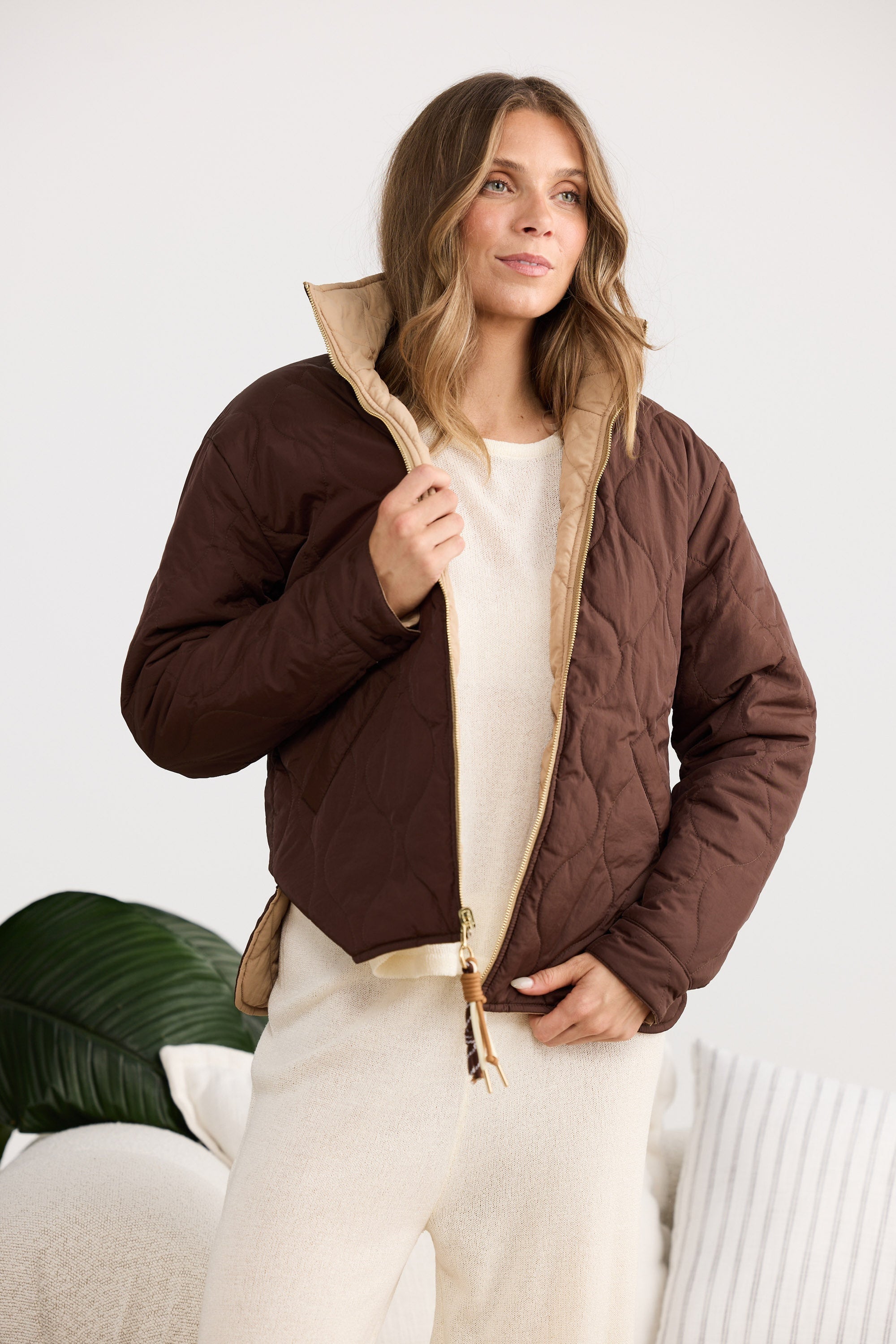 Woman wearing a brown quilted jacket with beige lining indoors.