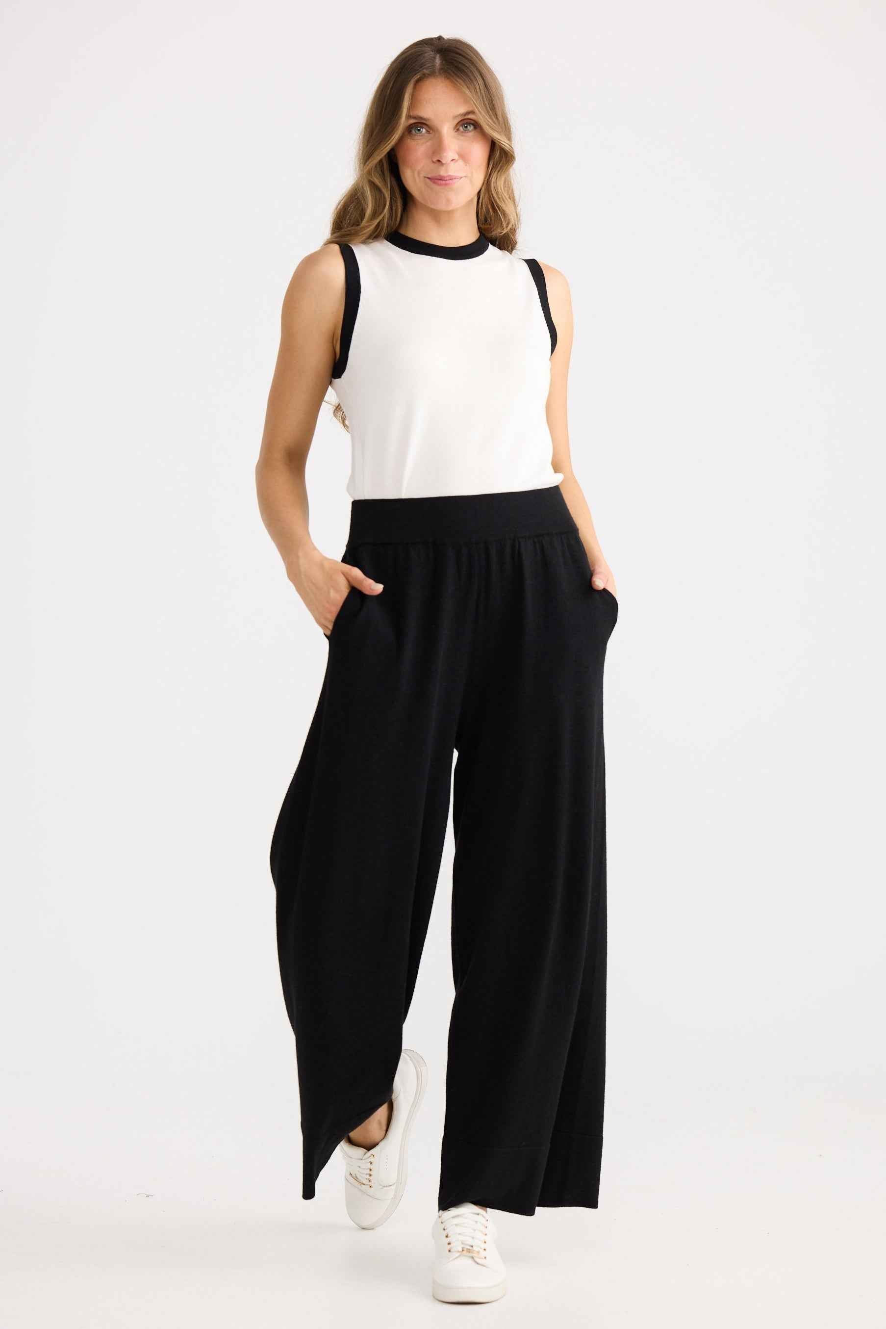 Woman wearing a white sleeveless top and black wide-leg pants on a white background