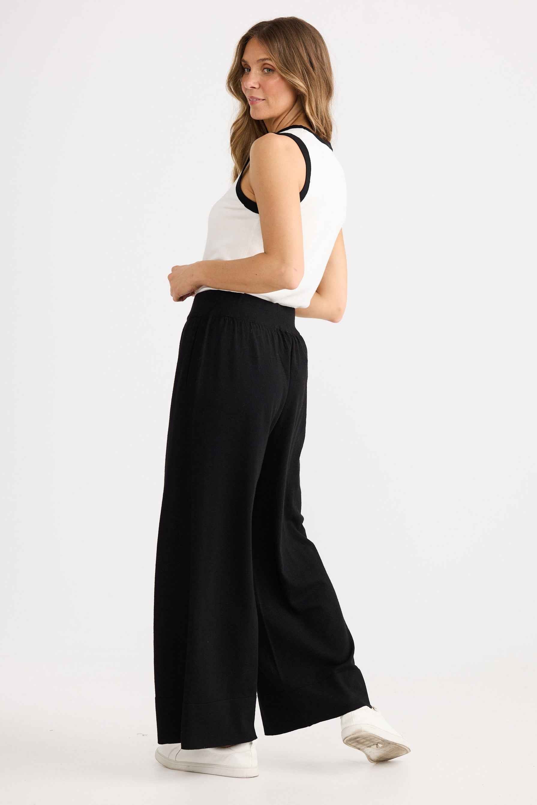 Woman wearing a white sleeveless top and black wide-leg pants on a white background