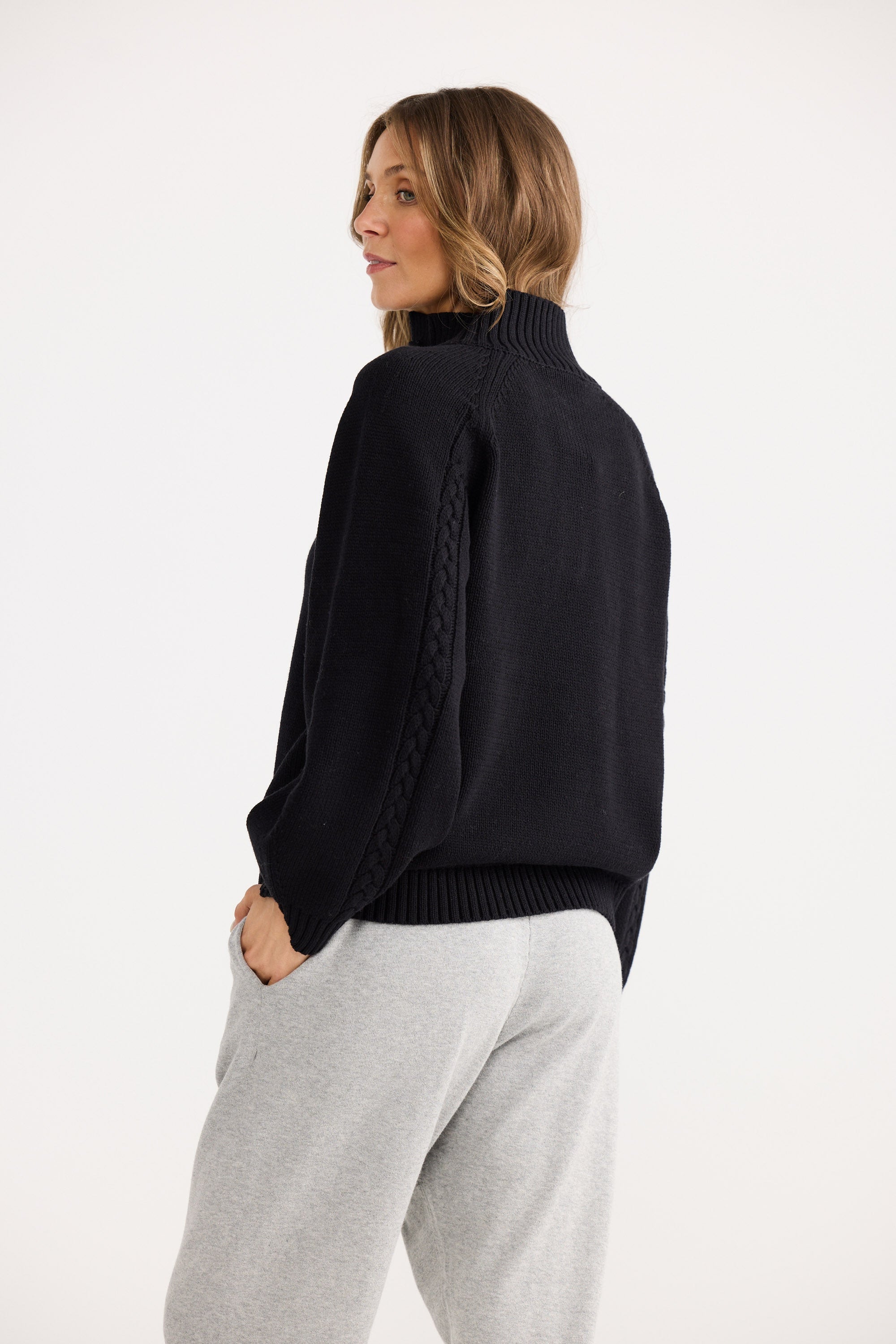 Woman wearing a black sweater and gray pants on a white background