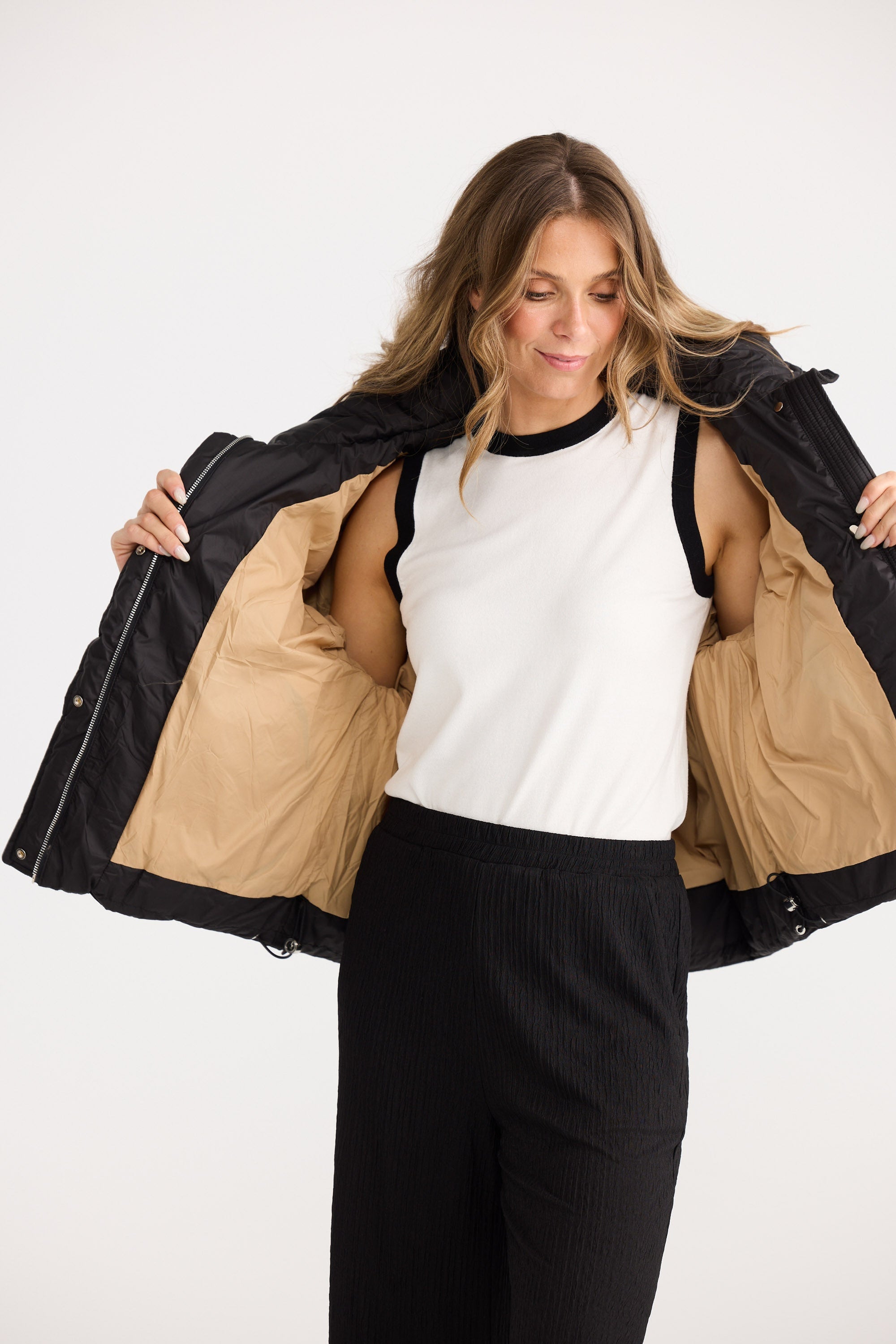 Woman wearing a black jacket with a beige interior, white shirt, and black pants on a white background