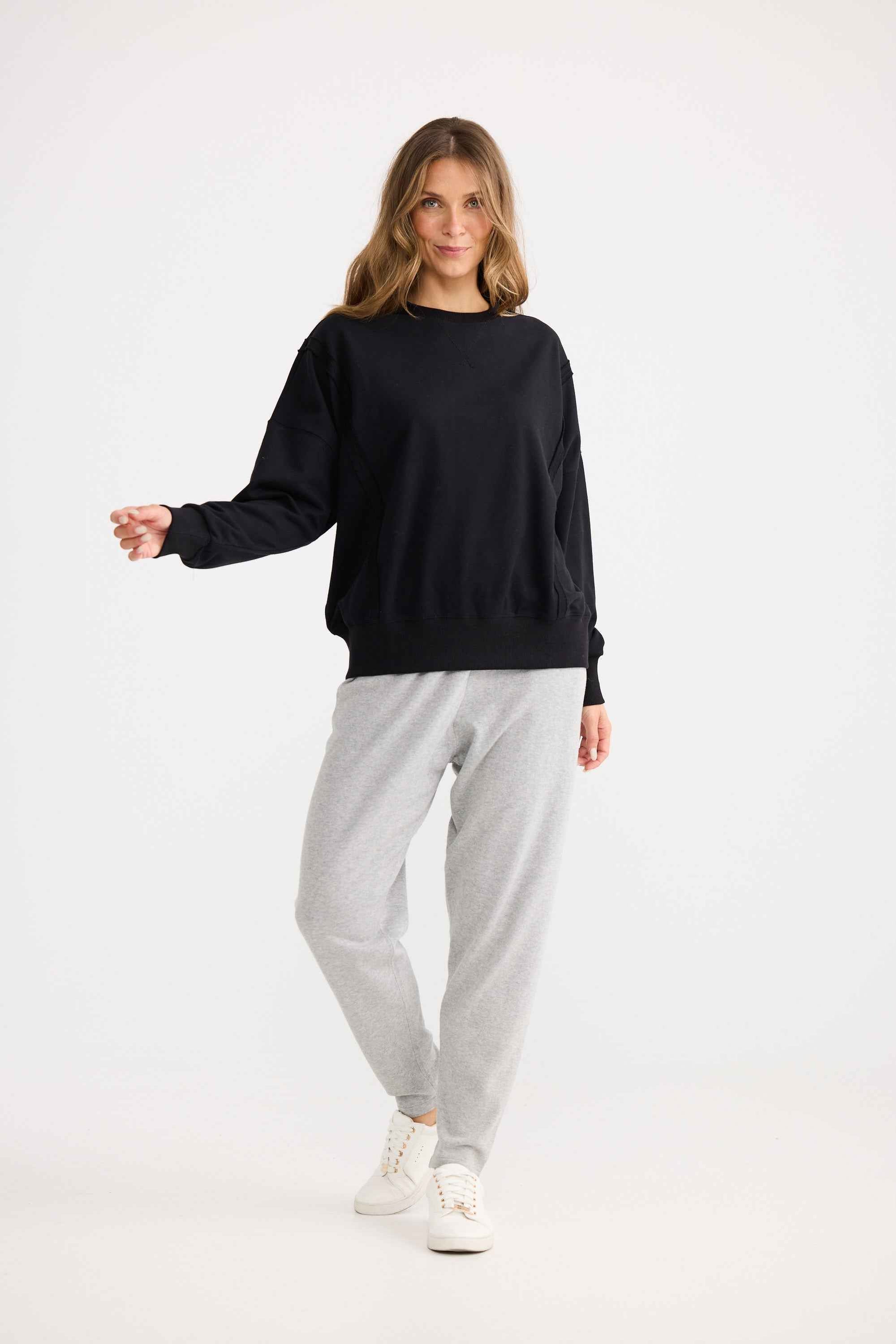 Woman wearing a black sweater and gray pants on a white background