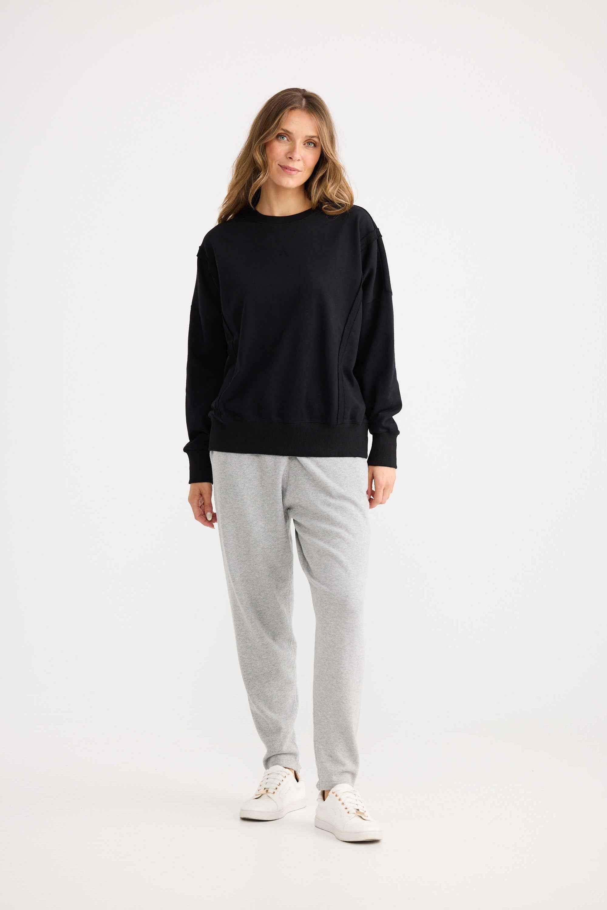 Woman wearing a black sweater and gray pants on a white background