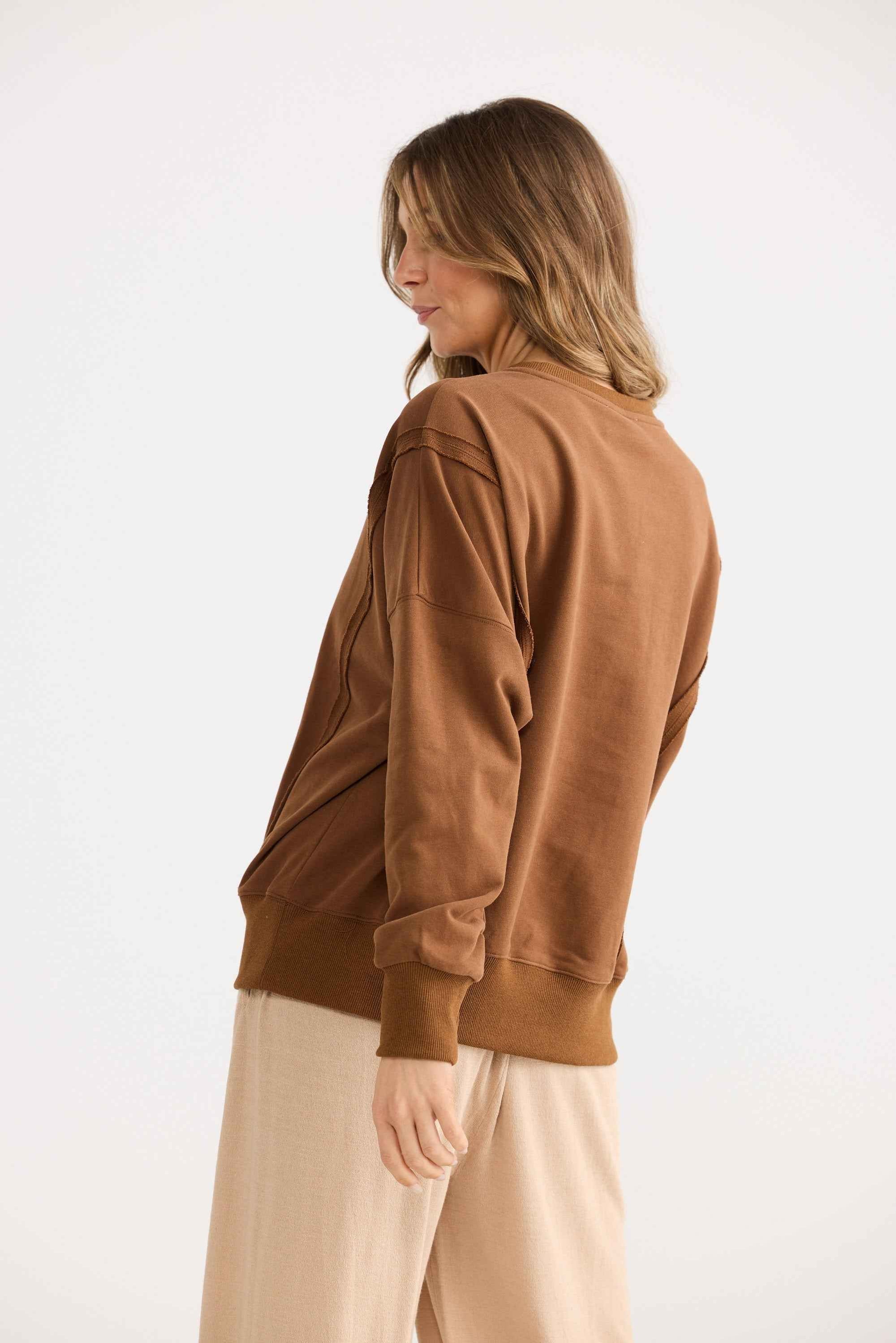 Woman wearing a brown jacket and beige pants on a white background