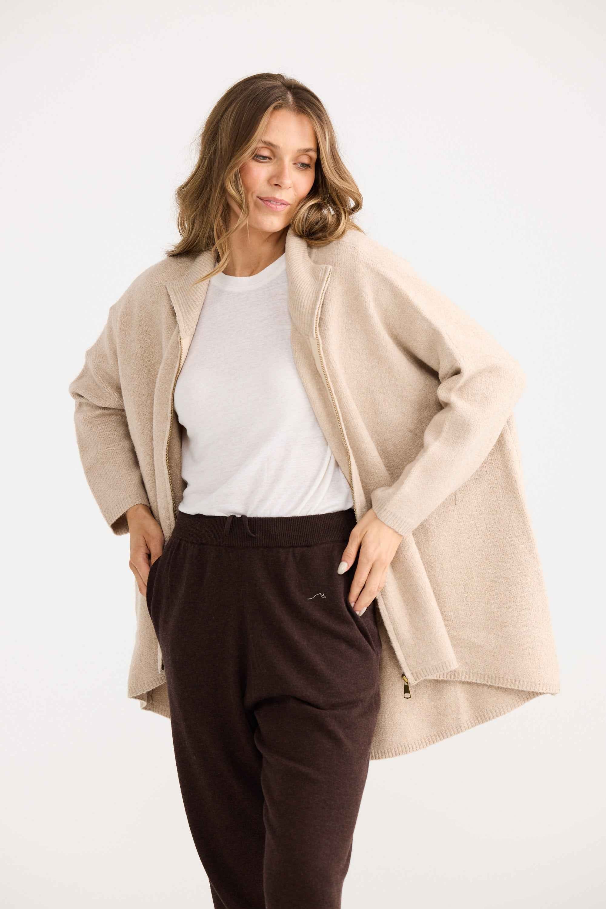 Woman wearing a beige cardigan over a white shirt and dark pants on a white background