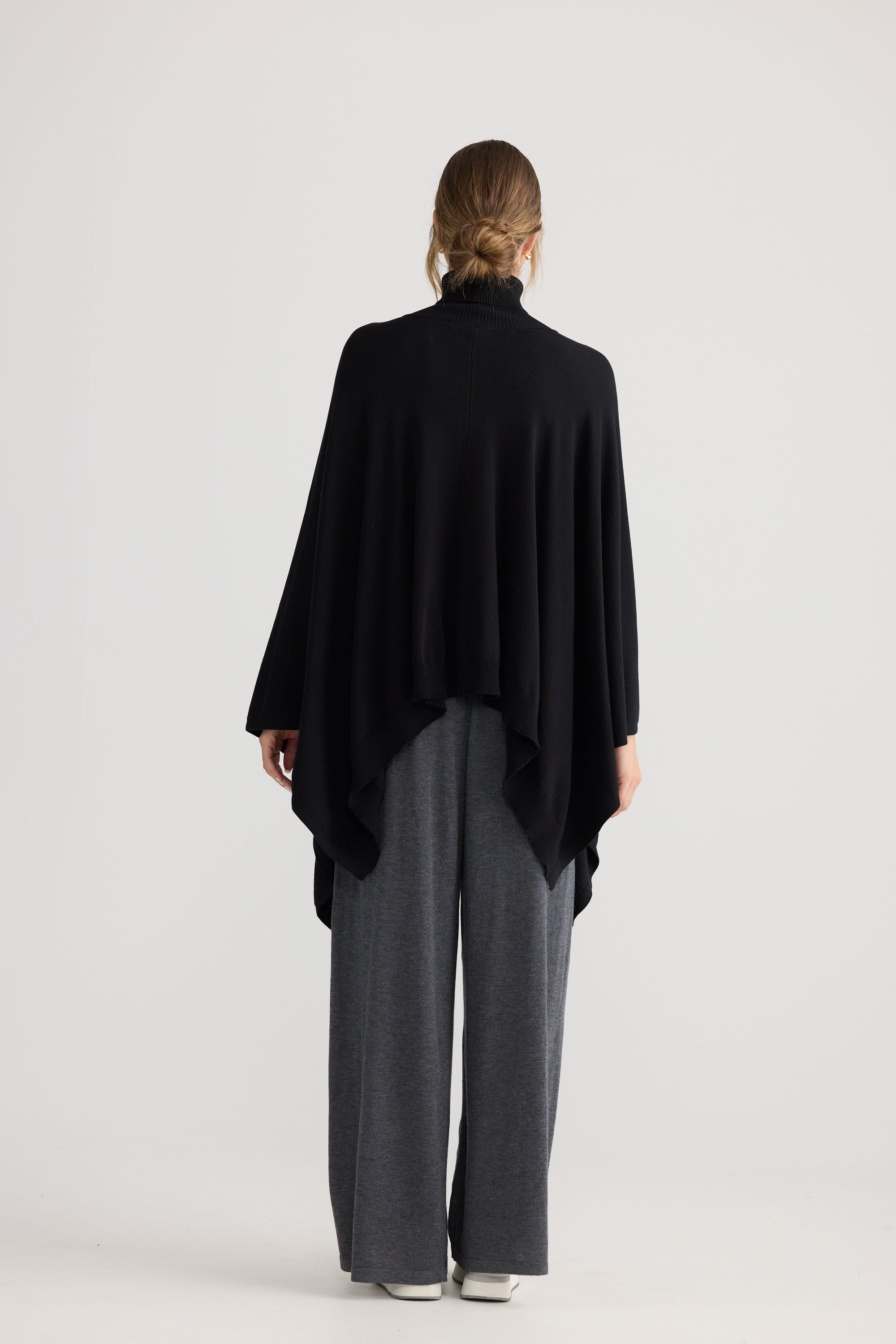 Awaken Knit Cape in black, styled with a relaxed outfit.